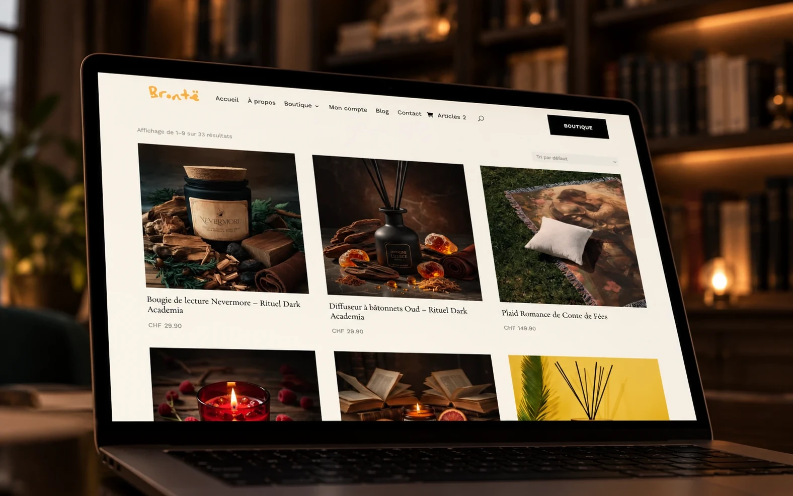 La boutique en ligne Brontë affichée sur un ordinateur portable, devant une bibliothèque : page du catalogue avec une bougie, un diffuseur et un plaid